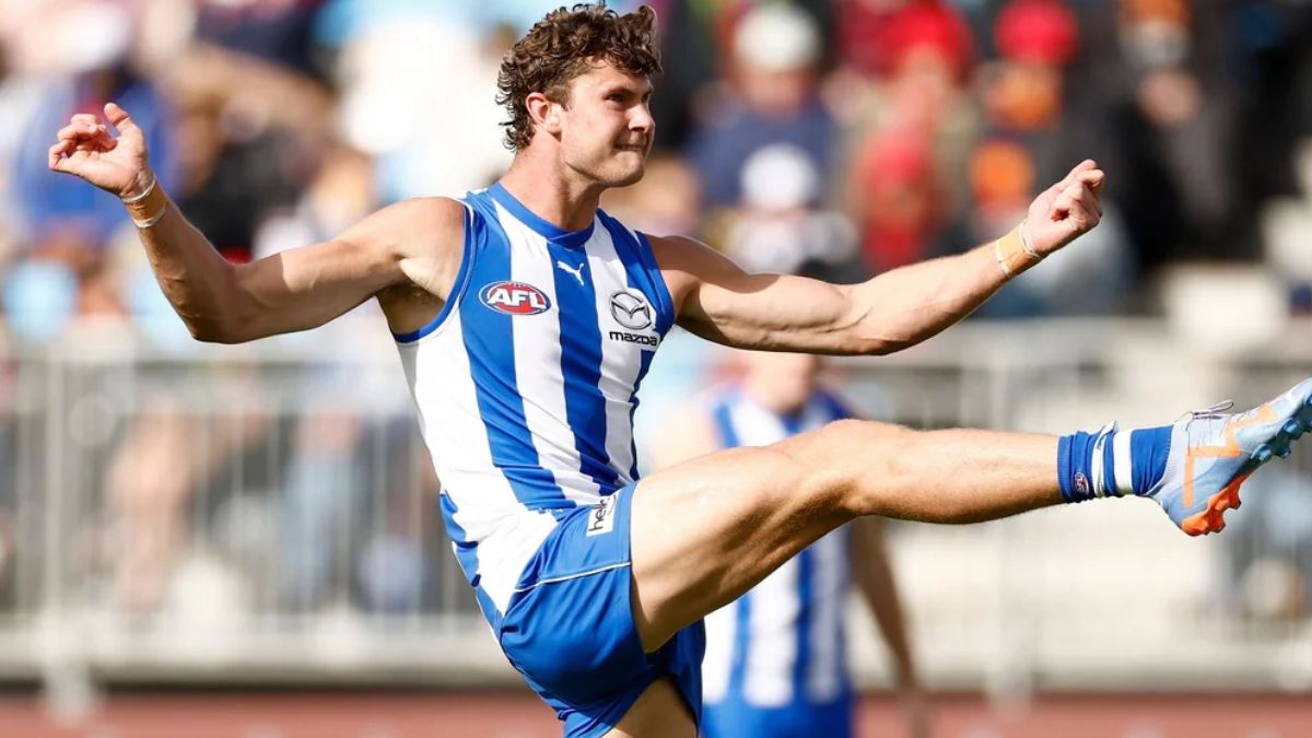 Australian rules footballer in a blue-and-white striped jersey mid-kick on the field, arm outstretched for balance.