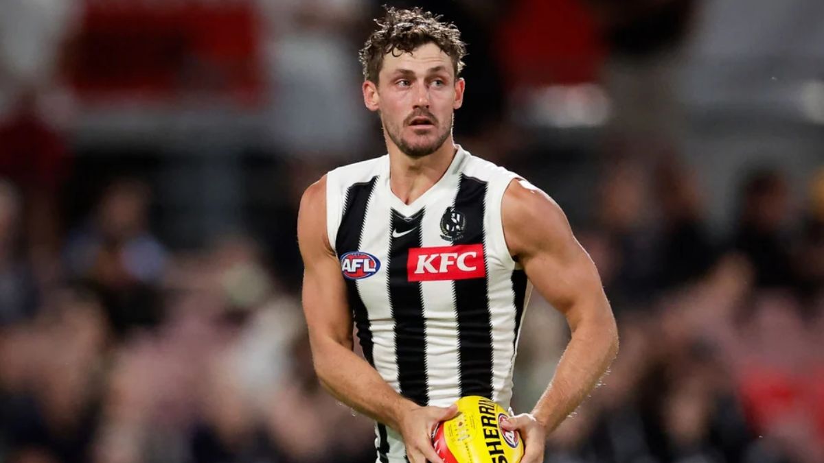 Australian rules footballer in a black-and-white striped jersey holding a yellow football on the field during a match, focused and ready to play.